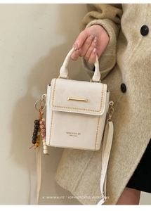 Detail of a cream faux leather handbag with gold metal bar and retro beaded charm