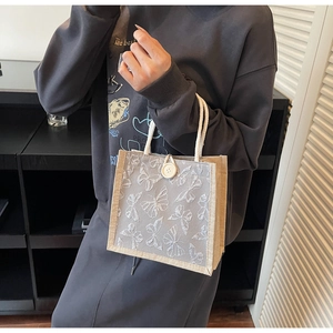 Detail of grey linen handbag featuring 3D butterfly embroidery and woven cotton handles