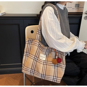 Detail of tartan plaid tote bag featuring a brown fluffy pompom and wide shoulder strap
