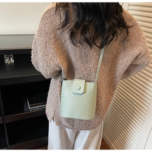Detail of light green woven bucket bag with magnetic snap and leather shoulder strap