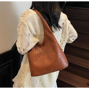 Detail of a brown woven tote bag featuring a glossy texture and silver metal clasp closure