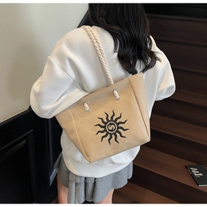 Close-up of beige linen tote bag with sun print and white rope handles through metal eyelets
