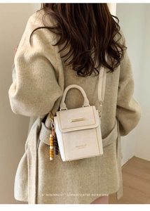 Close-up of beige leather mini crossbody bag with gold bar detail and wooden beads