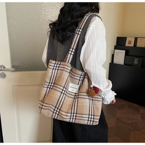 Detail of checkered tote bag featuring brown plaid pattern and plush ball charm accessory