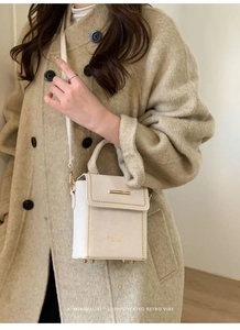 Detail of white PU leather crossbody bag featuring gold rivets and textured finish