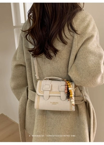 Detailed view of cream leather crossbody bag with beaded charm and double buckle closure