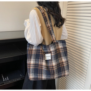 Detail of tartan tote bag featuring navy and orange plaid fabric with a brand patch