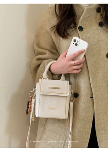 Close-up of white leather crossbody bag with gold accents and vintage wooden bead charm