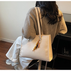 Close-up of off-white faux leather tote bag featuring a decorative wooden beaded charm