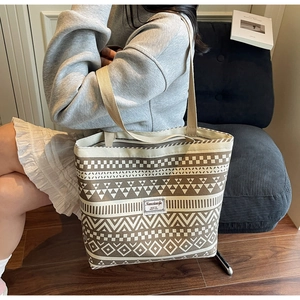 Close-up of cream canvas tote bag featuring brown geometric patterns and brand woven label