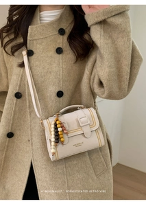 Detail of a beige leopard accent crossbody bag with wooden bead charm and flap buckle