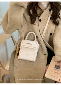 Chic beige crossbody bag with metal accent and wooden bead charm on a beige wool coat