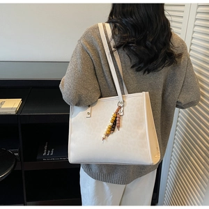 Detail of off-white tote bag with leopard embossing and colorful beaded tassel charm