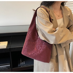 Detail of burgundy leopard print hobo bag in velvet texture worn with a trench coat