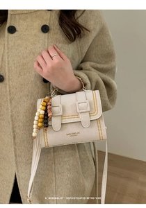 Detail of cream shoulder bag with yellow stitching and decorative wooden beads