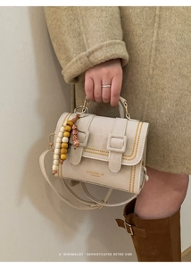 Close-up of creamy white designer handbag with yellow stitching and wooden bead charm