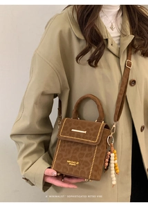 Detail of leopard print crossbody bag with gold hardware and beaded charm on a beige coat