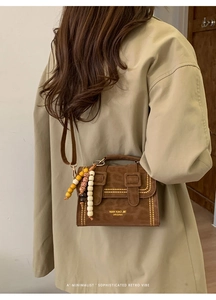 Close-up of brown vintage bag with stitching details and wooden bead charms on strap