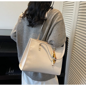 Detail of off-white PU leather tote bag with rivet accents and bohemian tassel charm