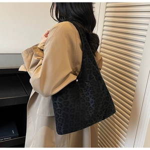 Detail of a large leopard print tote bag in velvet fabric worn with a khaki trench coat