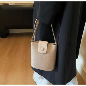 Detailed view of beige woven bucket bag with flap closure and circular buckle detail