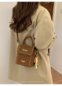 Detail of leopard print crossbody bag with gold studs and colorful beaded charm