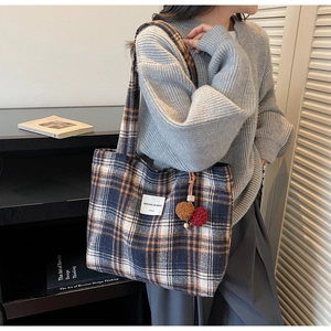 Detail of plaid tote bag with plush charms shown in a lifestyle interior setting