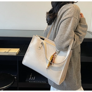 Detail of cream large tote bag with beaded charm accessory on shoulder of a model