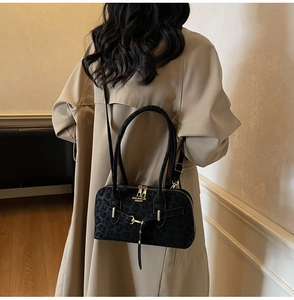 Detail of black leopard print suede crossbody bag with gold hardware on a beige coat