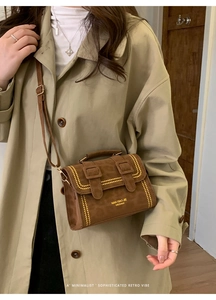 Close-up of vintage brown suede crossbody bag with double buckle and yellow stitching