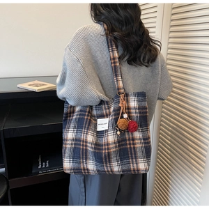 Detail of blue and orange plaid tote bag with plush ball charm for daily commute
