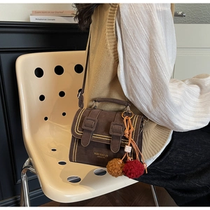 Nahaufnahme der braunen Wildleder-Satteltasche mit Goldnieten und farbigem Bommel