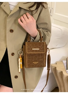 Detail of a brown leopard print crossbody bag with gold metal trim and beaded charm