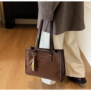 Detail of leopard print tote bag with brown leather handles and beaded charm accessory