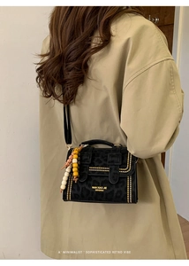 Detail of retro black suede handbag featuring leopard texture, gold studs, and beaded charm