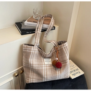 Detail of checkered tote bag with plush pom-poms on a light wood cabinet background