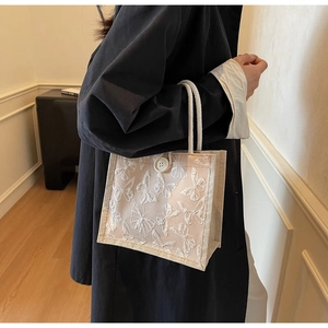 Detail of butterfly embroidery on beige woven handbag with rope handle and button closure