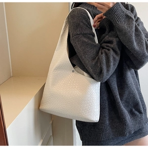 Close-up of white woven leather tote bag with metal rivets on a grey knit sweater