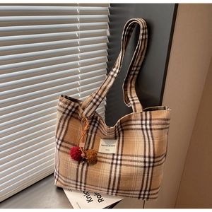 Detail of khaki plaid tote bag with plush pom-pom charm and fabric label in natural light