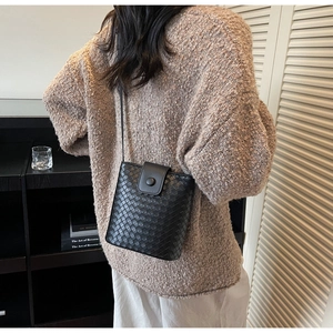 Detailed view of black woven crossbody bucket bag styled with a brown knit sweater
