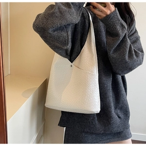 Detail of white woven tote bag with silver magnetic clasp on leather textured surface