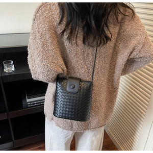 Detail of a black woven bucket bag with flap closure worn by a model in a stylish setting
