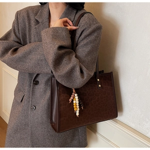 Detail of leopard print tote bag featuring bohemian bead charm and structured side seams