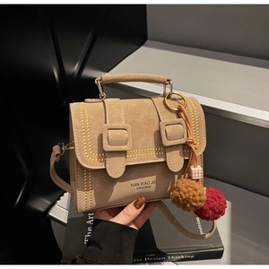 Detail der khakifarbenen Ledertasche mit Goldnieten und braunem Plüschkugel-Anhänger