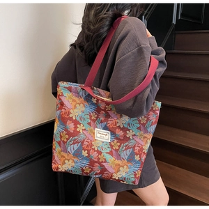 Detail of red jacquard tote bag with tropical flower patterns and wide burgundy shoulder strap
