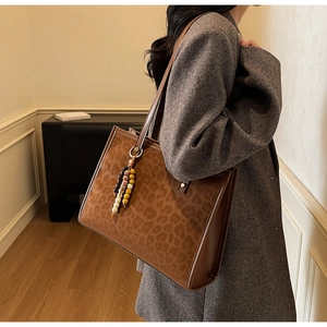 Detail of leopard print tote bag with ethnic beaded tassel and brown leather handle