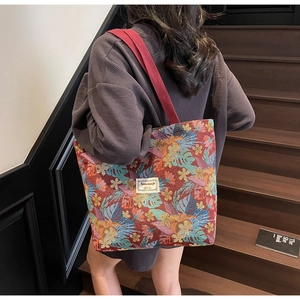 Ethnic style canvas tote bag with red floral print shown on model's shoulder in warm light