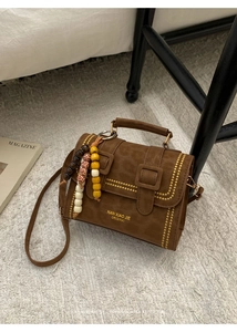 Detail of brown vintage suede crossbody bag with yellow studs and wood bead charm