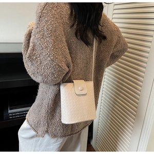 Detail of white woven texture bucket bag featuring flap closure and round decorative buckle