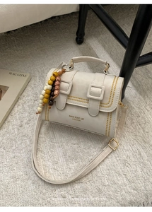 Detail of white mini bag featuring yellow stitching and wooden beaded charm decoration